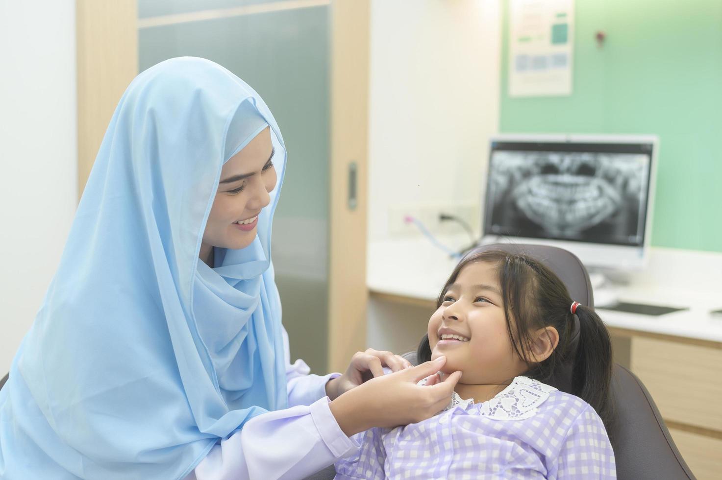 une petite fille mignonne ayant des dents examinées par un dentiste musulman dans une clinique dentaire, un contrôle des dents et un concept de dents saines photo