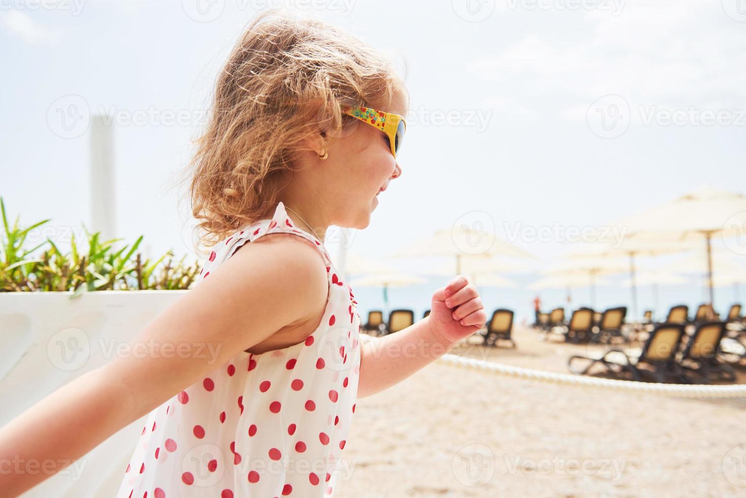 heureuse petite fille vêtue d'une robe sur la plage au bord de la mer en été. photo