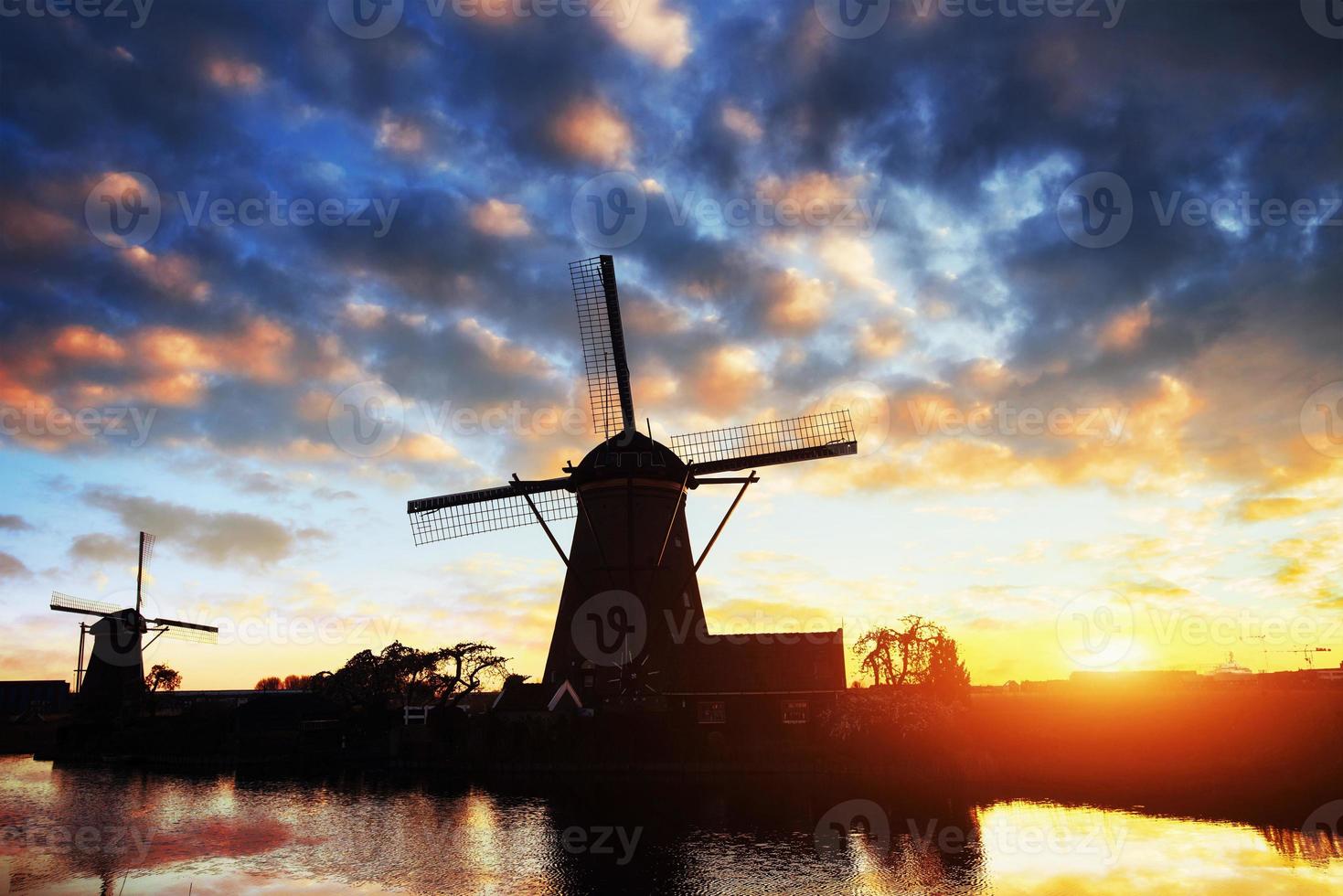 paysage avec beau moulin hollandais traditionnel près des cours d'eau avec coucher de soleil fantastique et reflet dans l'eau. Pays-Bas. photo