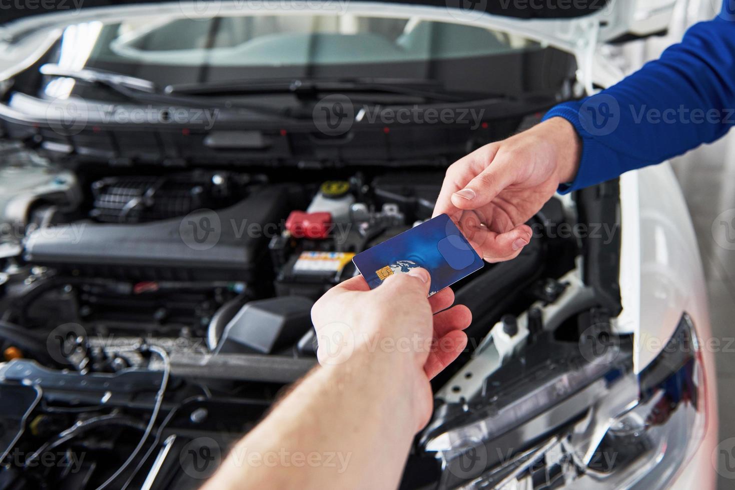 mains de mécanicien automobile avec clé dans le garage, paiement par carte de crédit photo