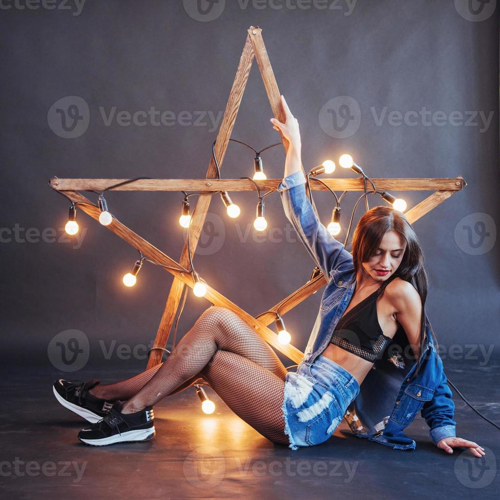 femme brune sexy en jeans sympa dans le studio. étoile en bois avec des lumières sur fond noir photo