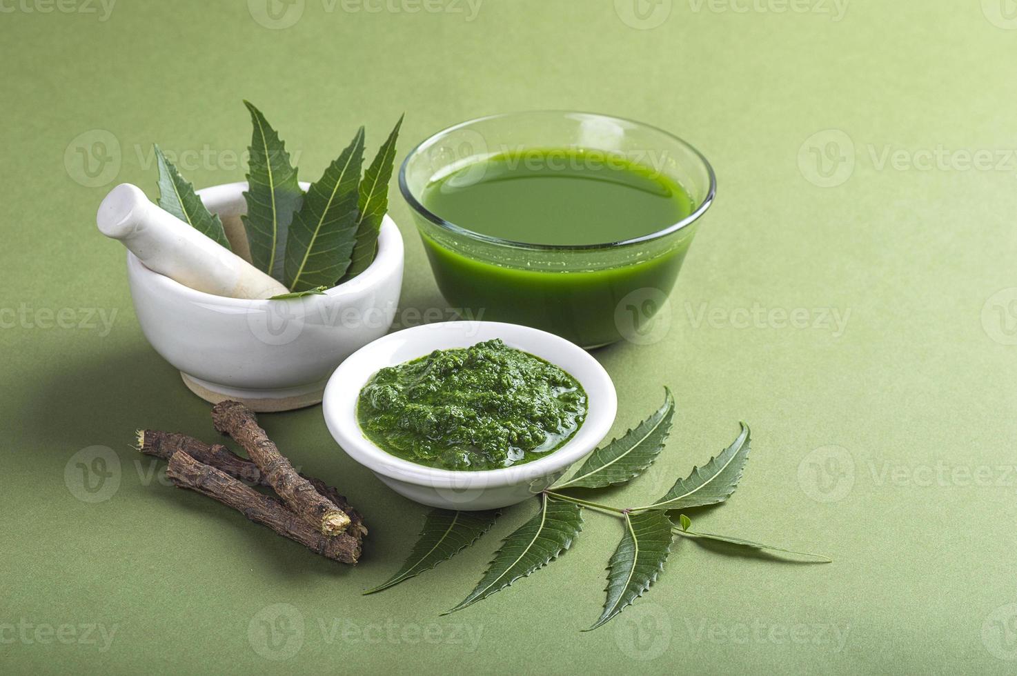 feuilles de neem médicinales dans un mortier et un pilon avec de la pâte de neem, du jus et des brindilles sur fond vert photo