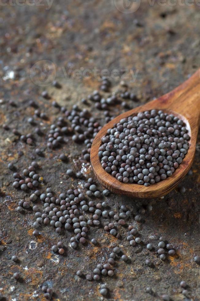 graines de moutarde brunes dans une cuillère en bois sur un fond texturé photo