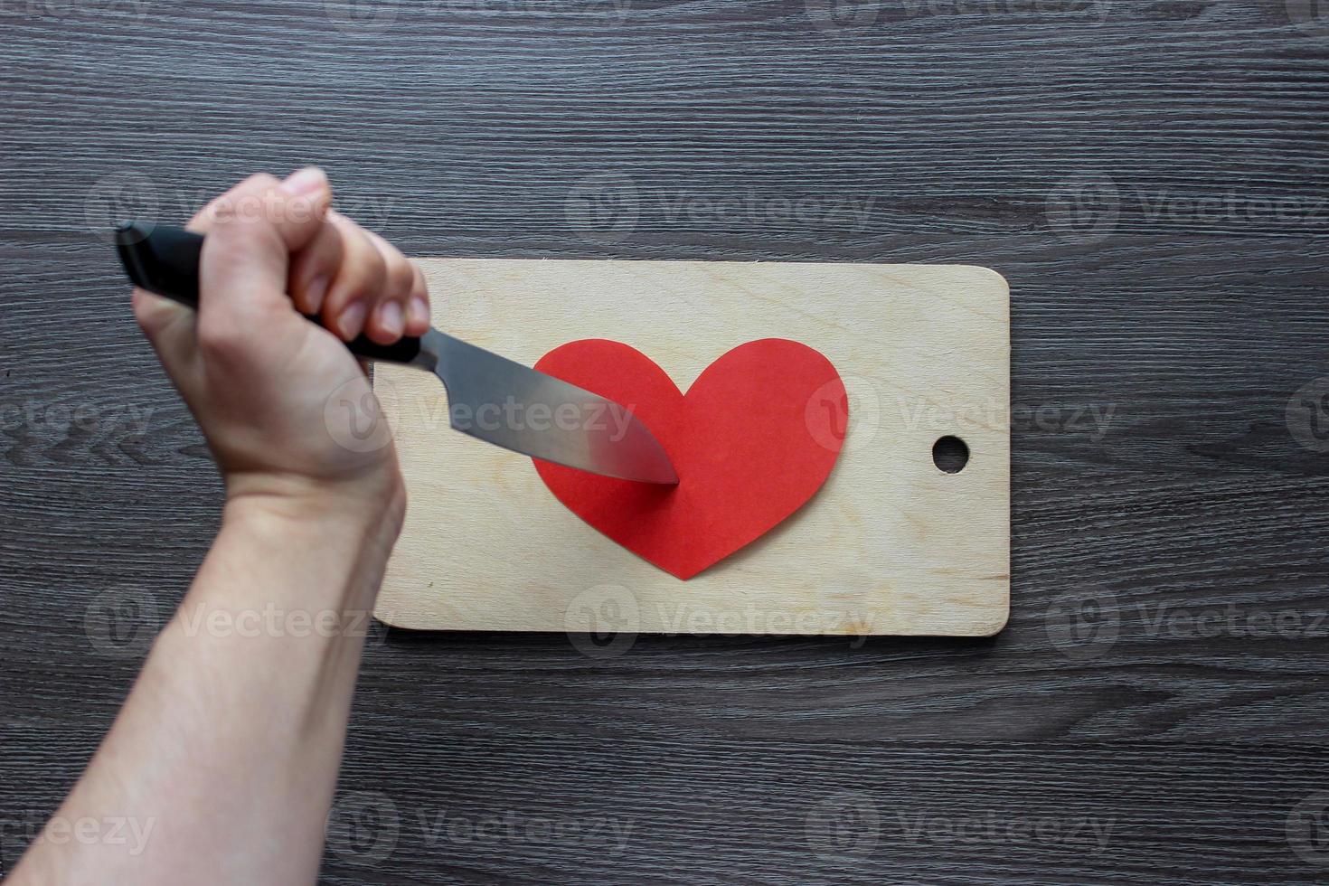 main avec un couteau coupant un coeur de papier sur une planche à découper photo