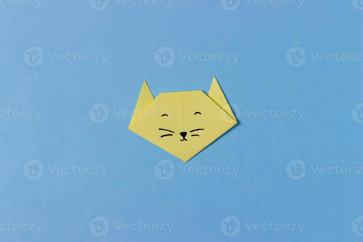 la tête du chat est pliée à partir de papier jaune dans la technique de l'origami avec des yeux, un nez et une moustache peints. au milieu du fond bleu. photo