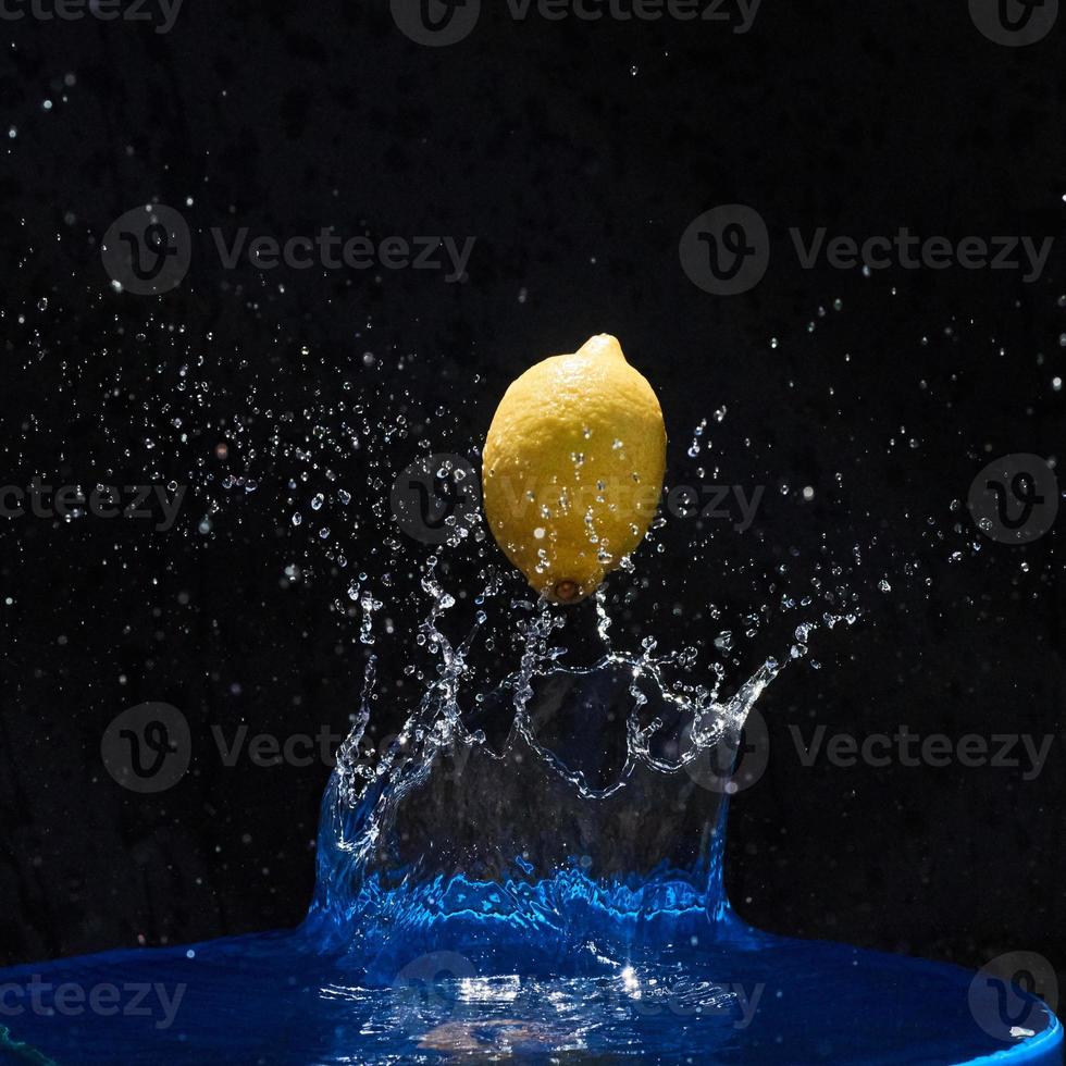 citron jaune juteux tombe dans l'eau sur fond noir photo