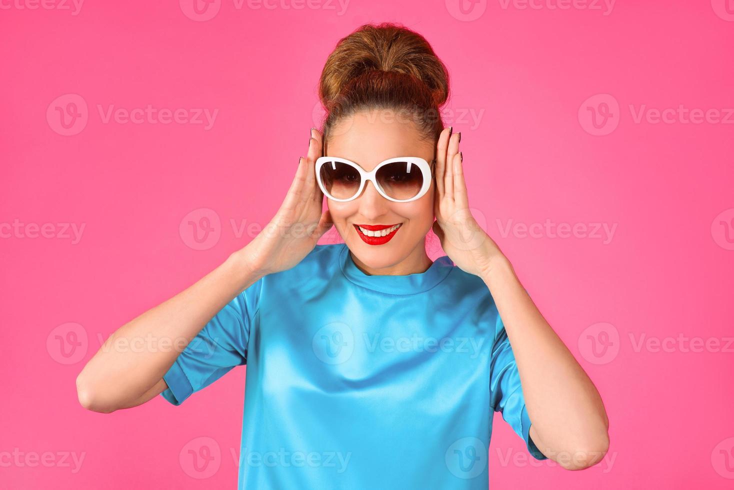 portrait de jeune belle femme en robe de soie bleue et lunettes de soleil blanches sur fond rose photo