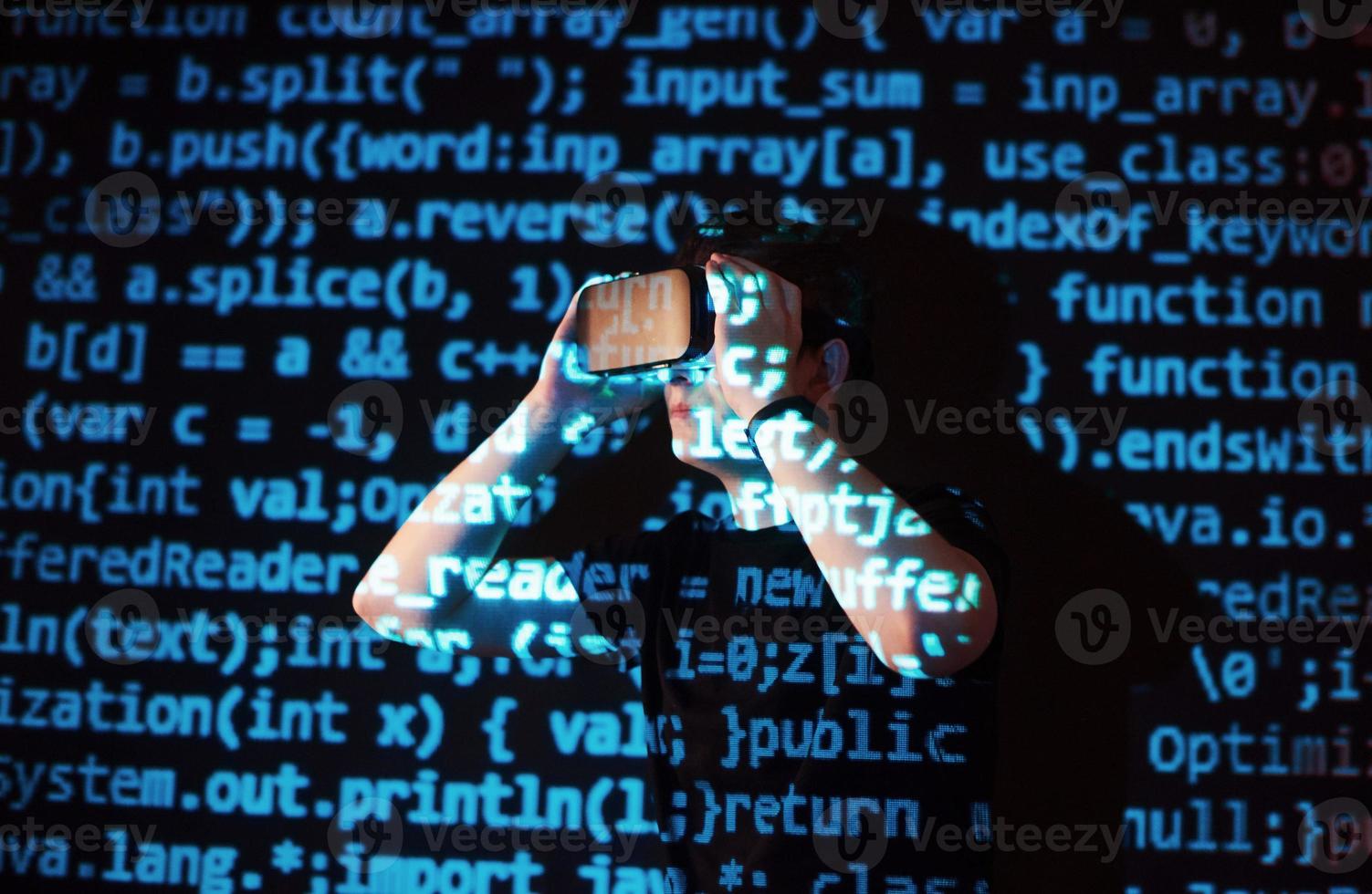 la double exposition d'un homme caucasien et d'un casque de réalité virtuelle est vraisemblablement un joueur ou un pirate qui craque le code dans un réseau ou un serveur sécurisé, avec des lignes de code photo