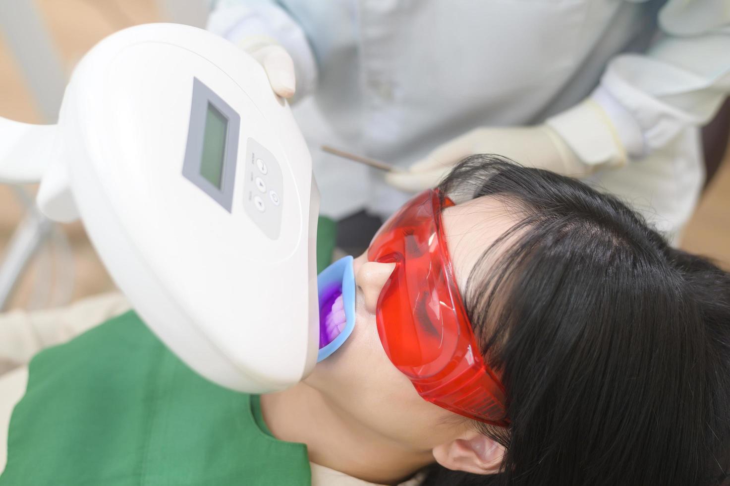 une femme portant des lunettes de protection examinant par stomatologue , blanchiment des dents par lampe ultraviolette photo