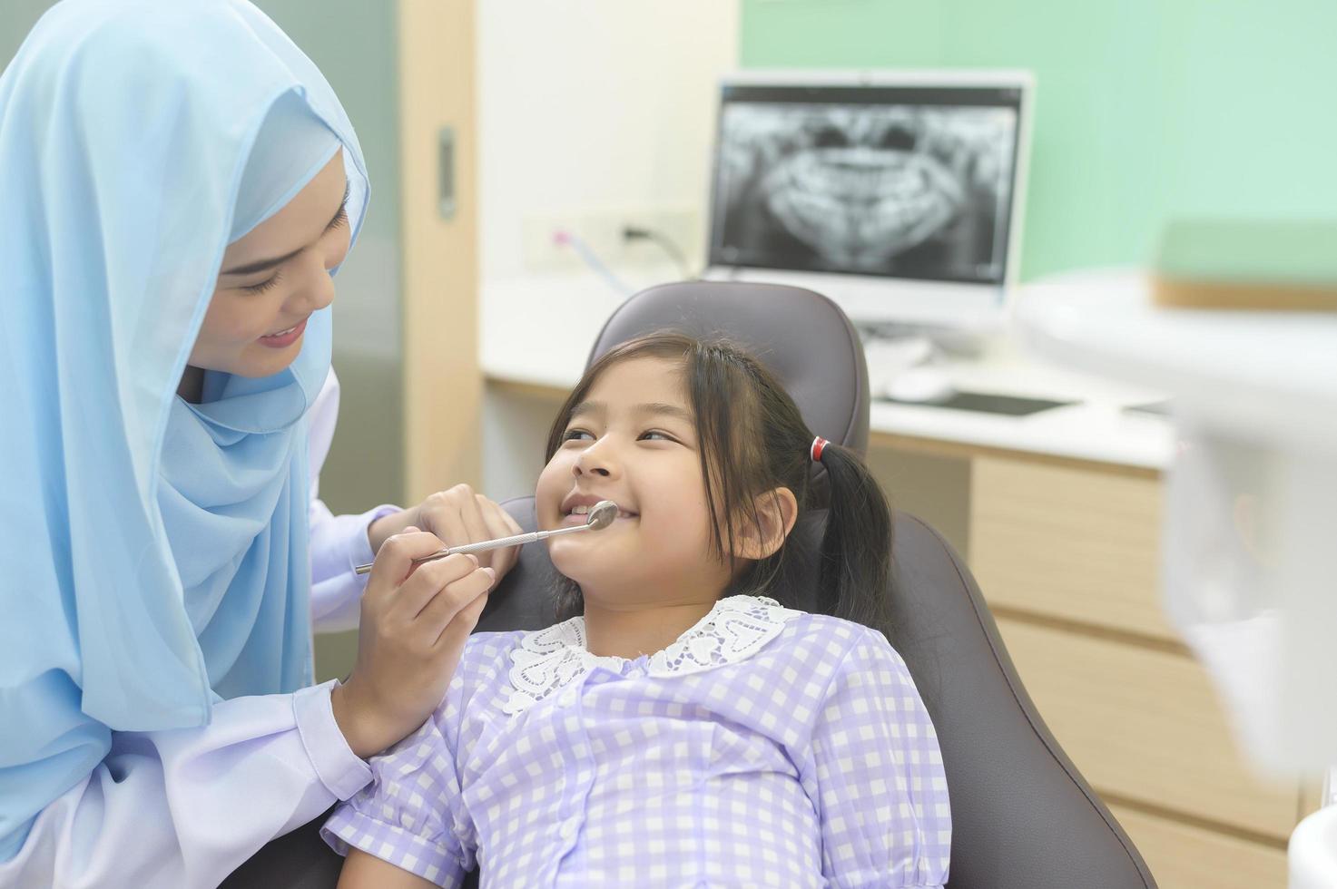 une petite fille mignonne ayant des dents examinées par un dentiste musulman dans une clinique dentaire, un contrôle des dents et un concept de dents saines photo