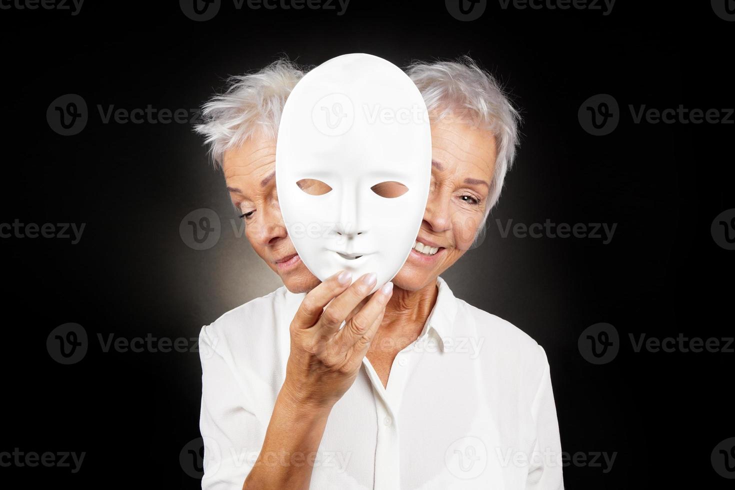 femme plus âgée cachant un visage heureux et triste derrière un masque photo