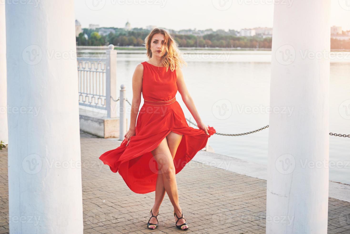 heureuse belle jeune femme dansant de liberté en été avec lac en arrière-plan. contraste des couleurs rouge et blanc photo