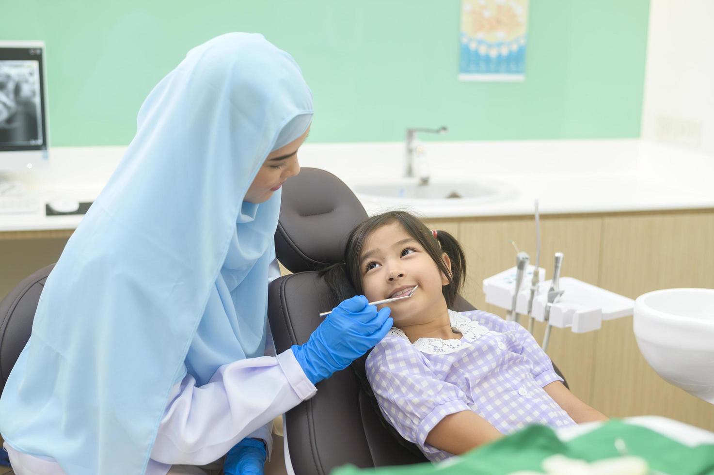 une petite fille mignonne ayant des dents examinées par un dentiste musulman dans une clinique dentaire, un contrôle des dents et un concept de dents saines photo