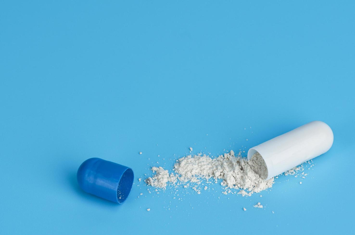 gros plan capsule de médecine ouverte pilule avec de la poudre sur fond bleu. photo