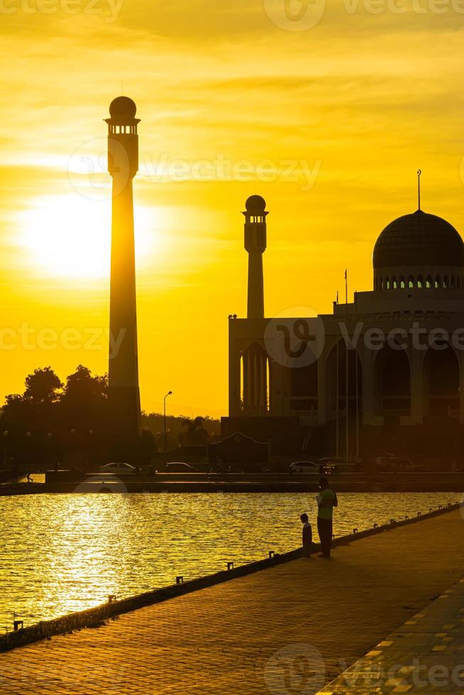 mosquée centrale de songkhla de jour comme de nuit avec un ciel coloré au coucher du soleil et les lumières de la mosquée et des reflets dans l'eau dans un concept de paysage emblématique photo