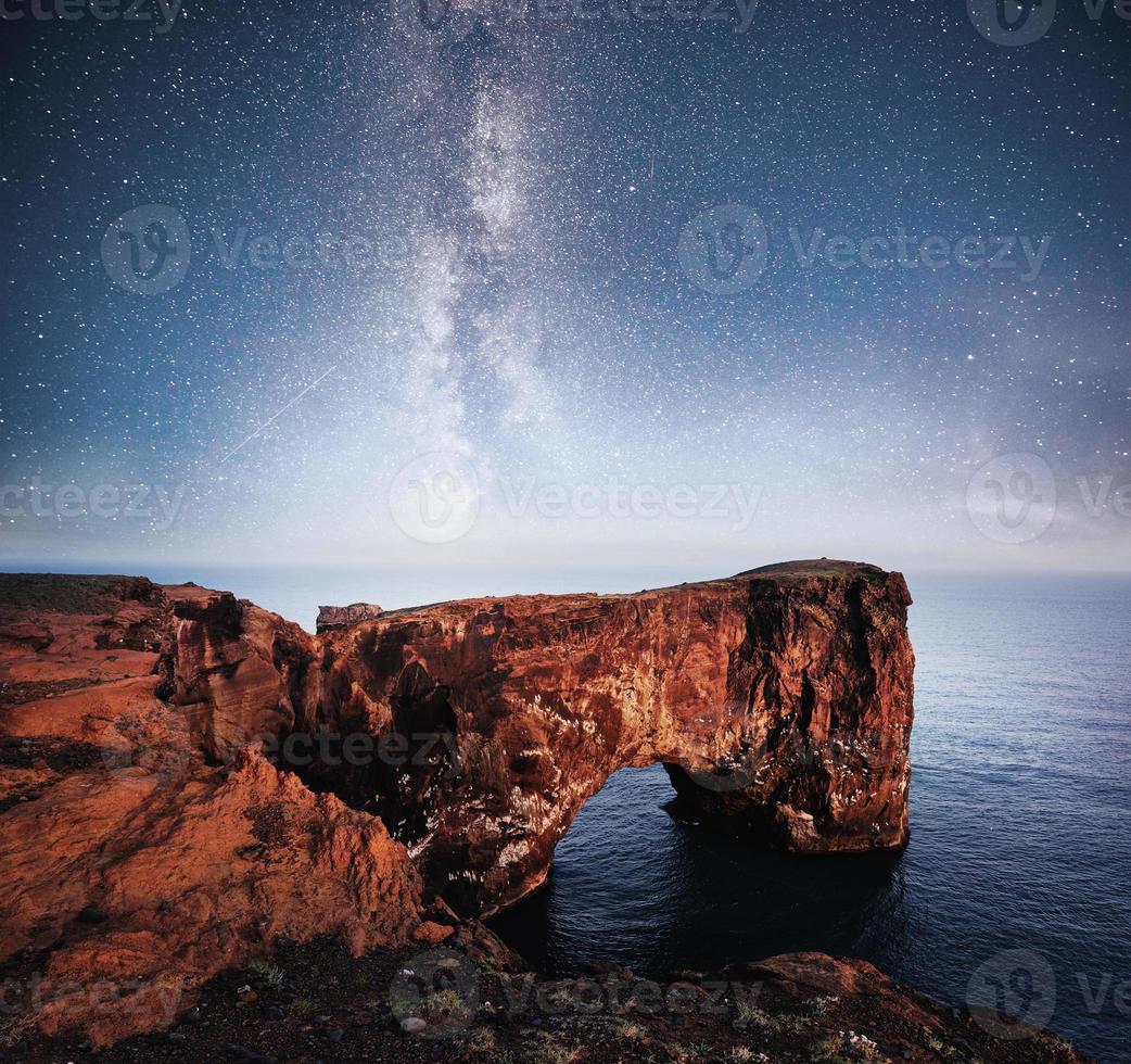 cap dyrholaey au sud de l'islande. altitude 120 m, et îlot de colline moyenne avec une porte ouvrante. ciel nocturne vibrant avec étoiles et nébuleuse et galaxie. astrophoto du ciel profond photo