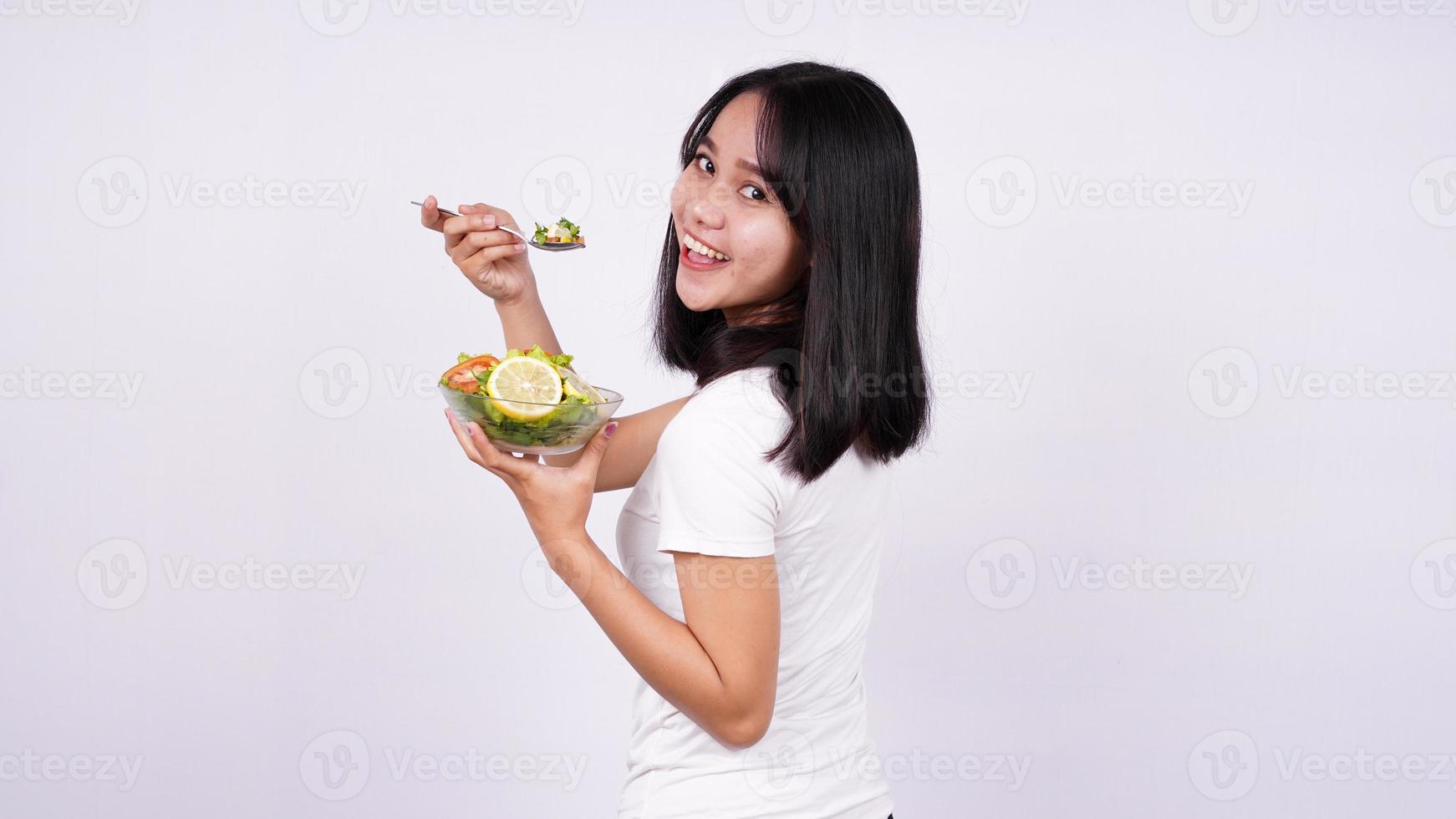 jeune femme asiatique heureuse de manger une salade saine avec un fond blanc isolé photo