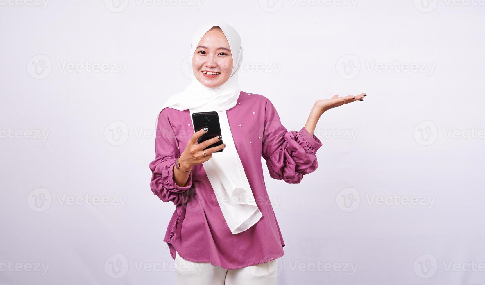 belle femme hijab pointant vers la zone et maintenez le téléphone isolé sur fond blanc photo