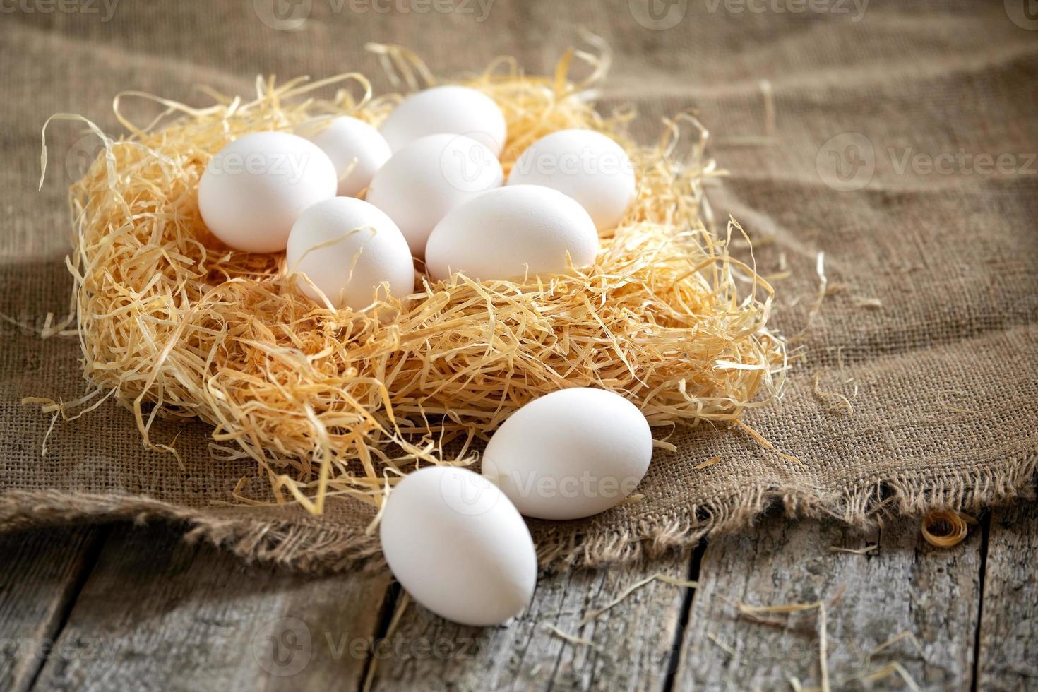 oeufs de poule blancs dans le nid de paille sur une toile de jute sur des planches en bois photo