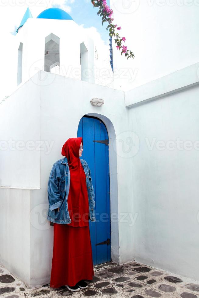 femme musulmane posant sur la porte en bois bleue traditionnelle de santorin et les dômes bleus photo