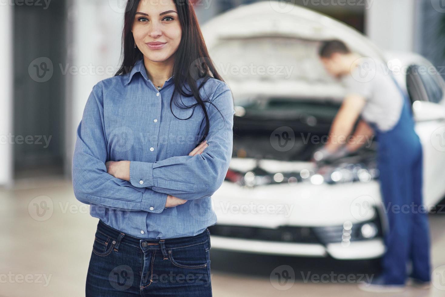 femme dans un garage automobile obtenant un service mécanique. le mécanicien travaille sous le capot de la voiture photo