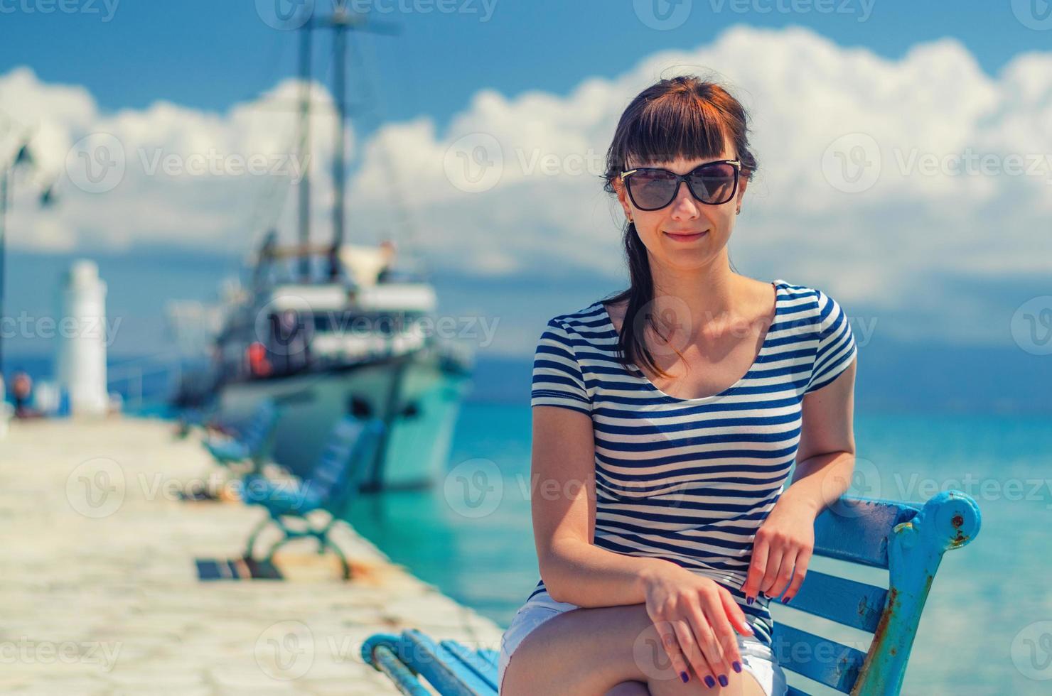 belle jeune fille avec t-shirt rayé et lunettes de soleil sourire et s'asseoir sur un banc dans la jetée photo