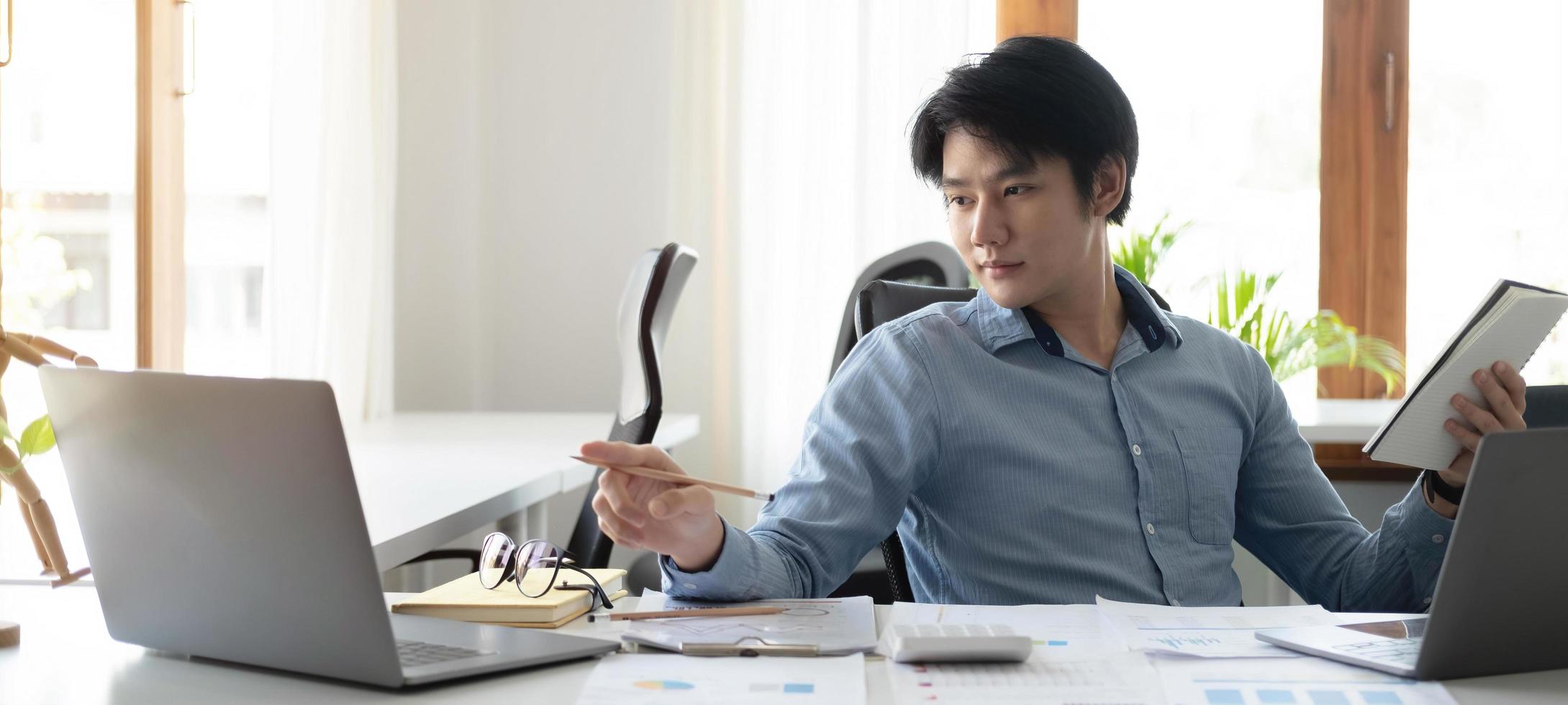 portrait d'un jeune homme asiatique pigiste à la main travaille son travail sur une tablette informatique dans un bureau moderne. faire un rapport d'analyse comptable sur les données d'investissement immobilier, le concept de systèmes financiers et fiscaux. photo