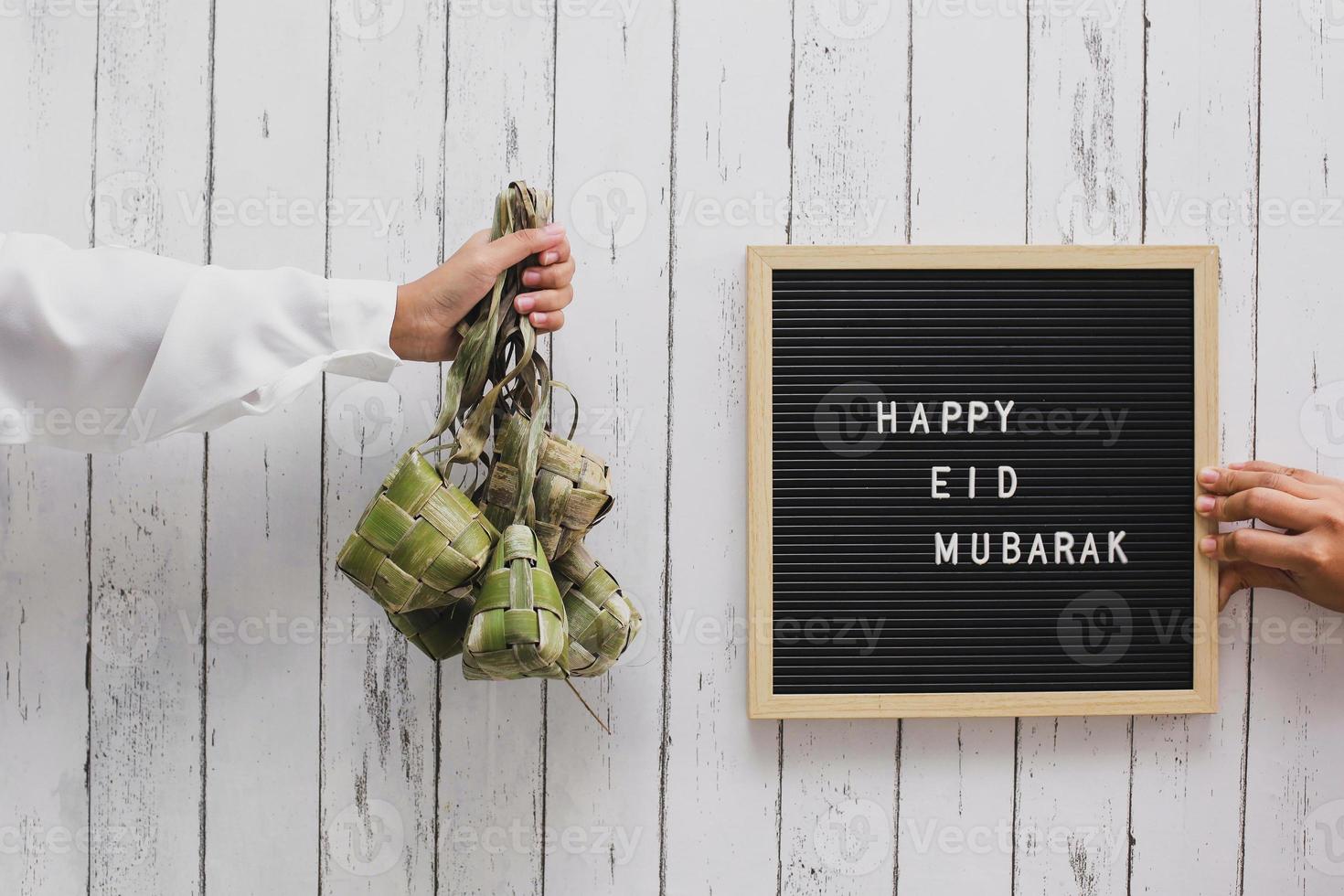 main tenant un gâteau de riz en indonésie appelé ketupat et le tableau des lettres dit joyeux eid mubarak photo