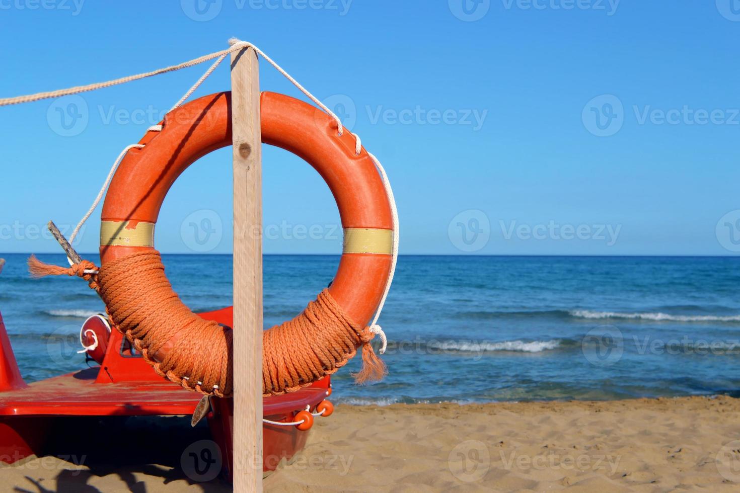 bouée de sauvetage en bord de mer. équipement de sauvetage de personnes. service de sauvetage.arbre avec gilet de sauvetage orange sur la plage au bord de la mer.paysage marin avec, avec ciel bleu et plage de sable. photo