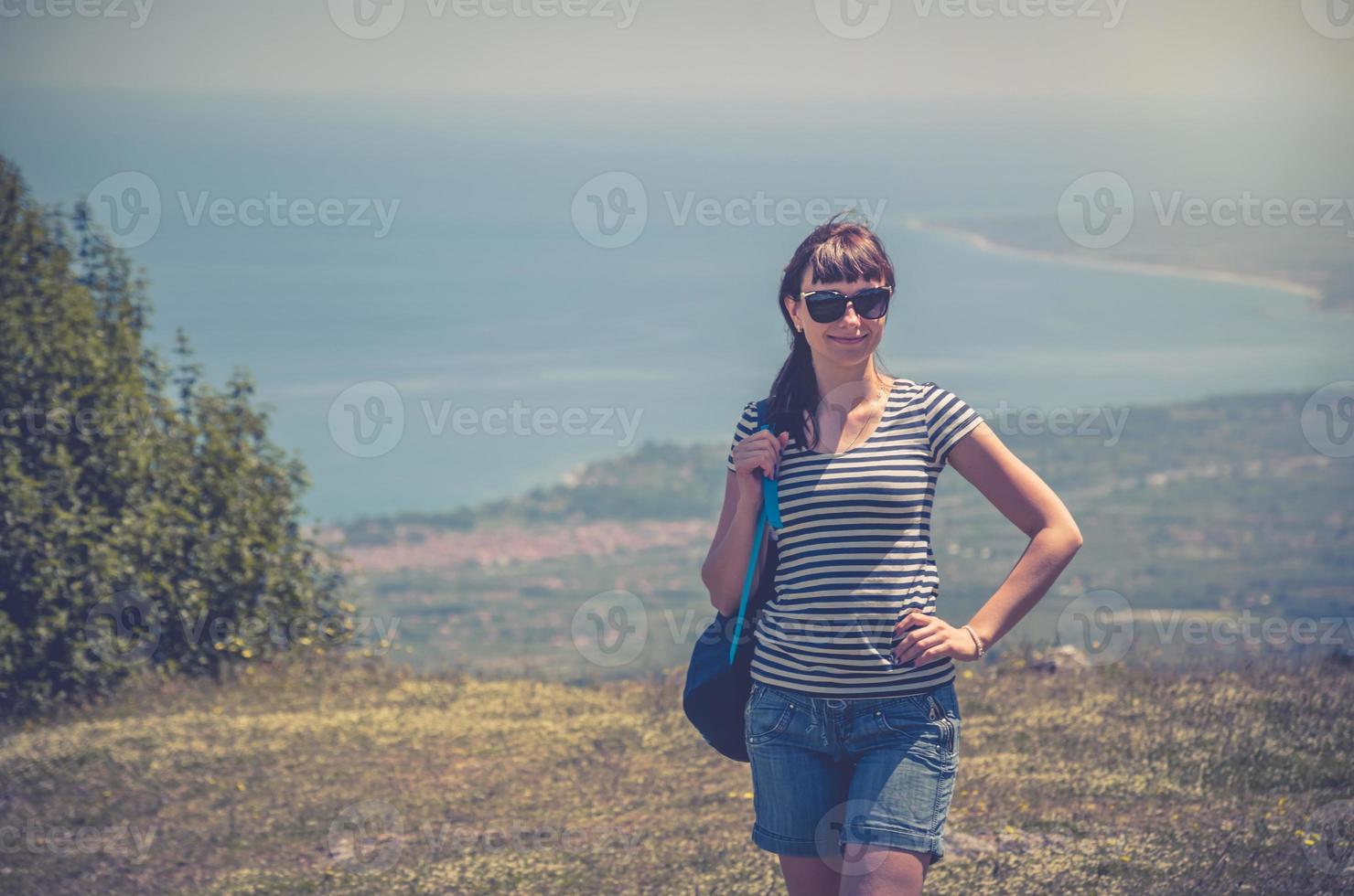 jeune belle fille voyageur avec chemise rayée, sac à dos et lunettes de soleil regardant la caméra photo