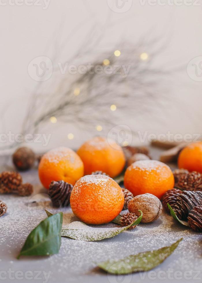 mandarines orange sur fond gris dans le décor du nouvel an avec des pommes de pin brunes et des feuilles vertes. décoration de noël avec des mandarines. délicieuse clémentine sucrée. photo