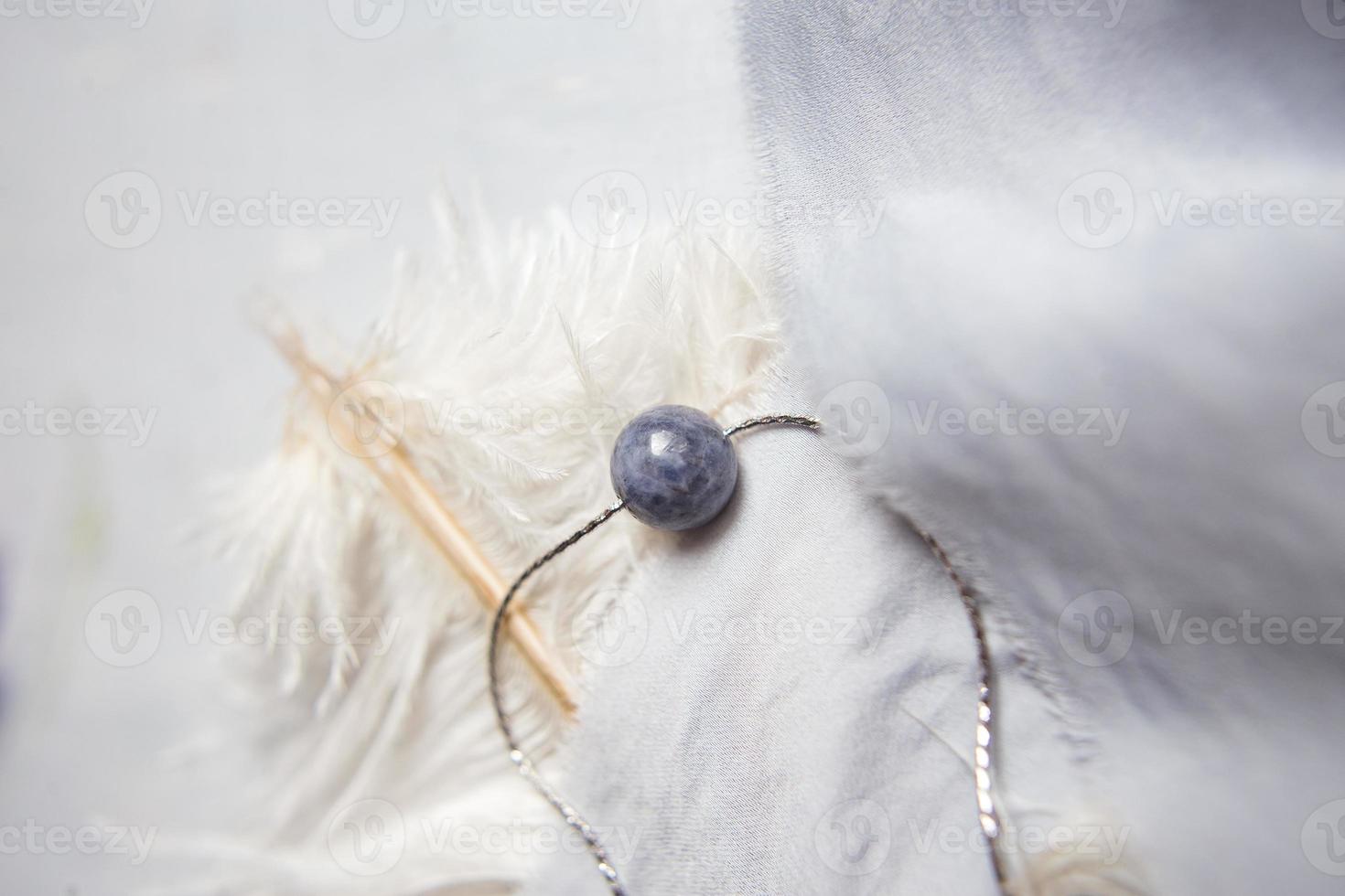 collier en pierre naturelle avec garnitures en argent avec des fleurs de lilas violet violet sur une plume d'autruche blanche. accessoires en argent. photo