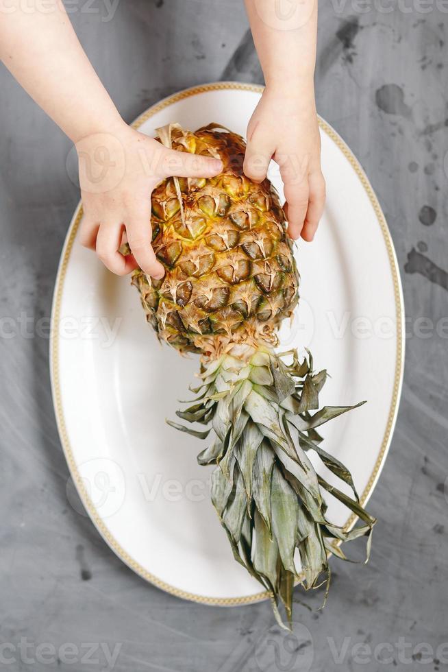 assiette blanche avec ananas entier mûr sur fond de béton gris. photo