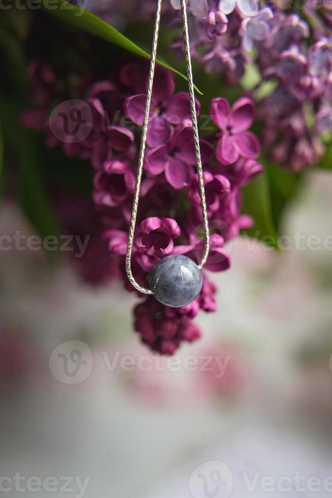 collier en pierre naturelle avec garnitures en argent avec des fleurs de lilas violet violet sur une plume d'autruche blanche. accessoires en argent. photo