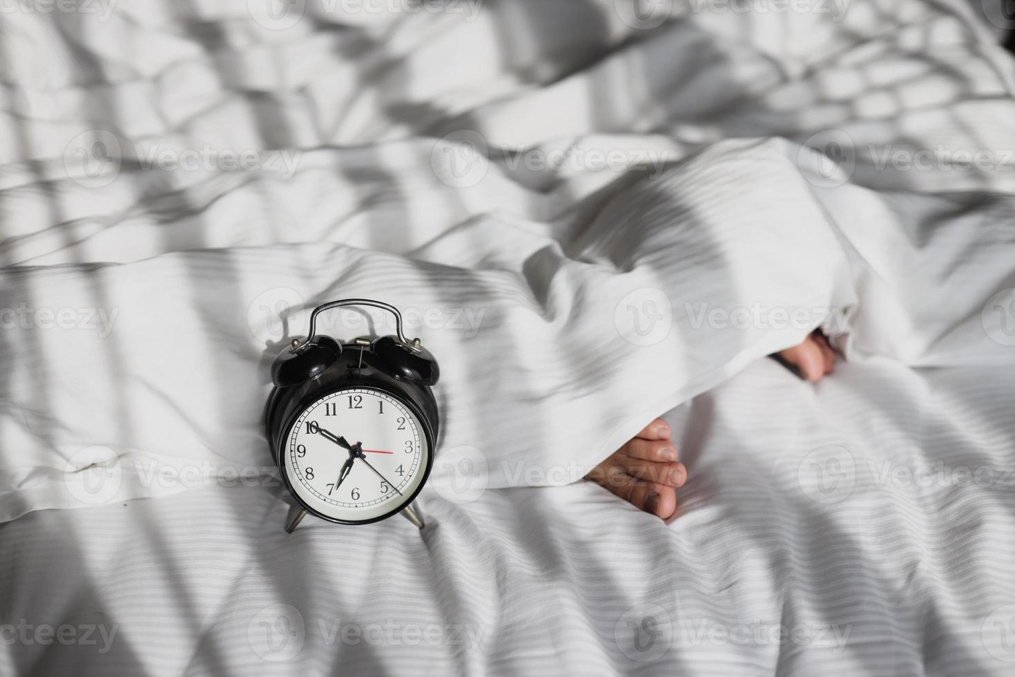 réveil montrant 7 heures sur le lit avec les pieds d'une personne endormie sur une couverture le matin photo