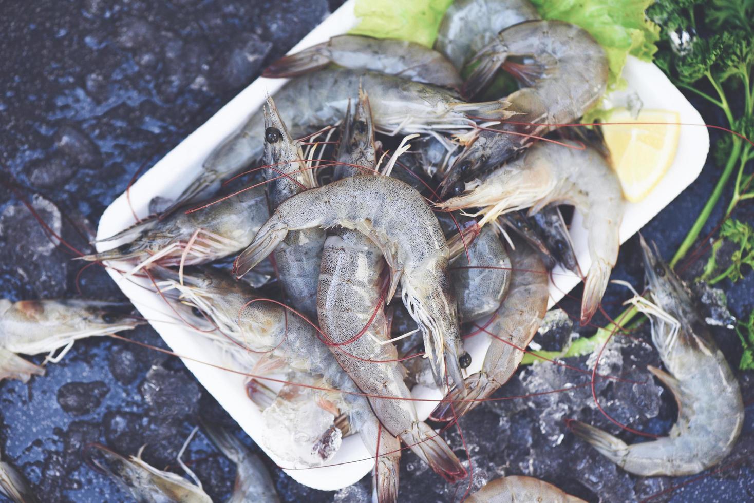 crevettes crues sur plateau en plastique, crevettes fraîches pour la cuisson aux épices salade de légumes au citron laitue sur fond sombre dans le restaurant de fruits de mer photo