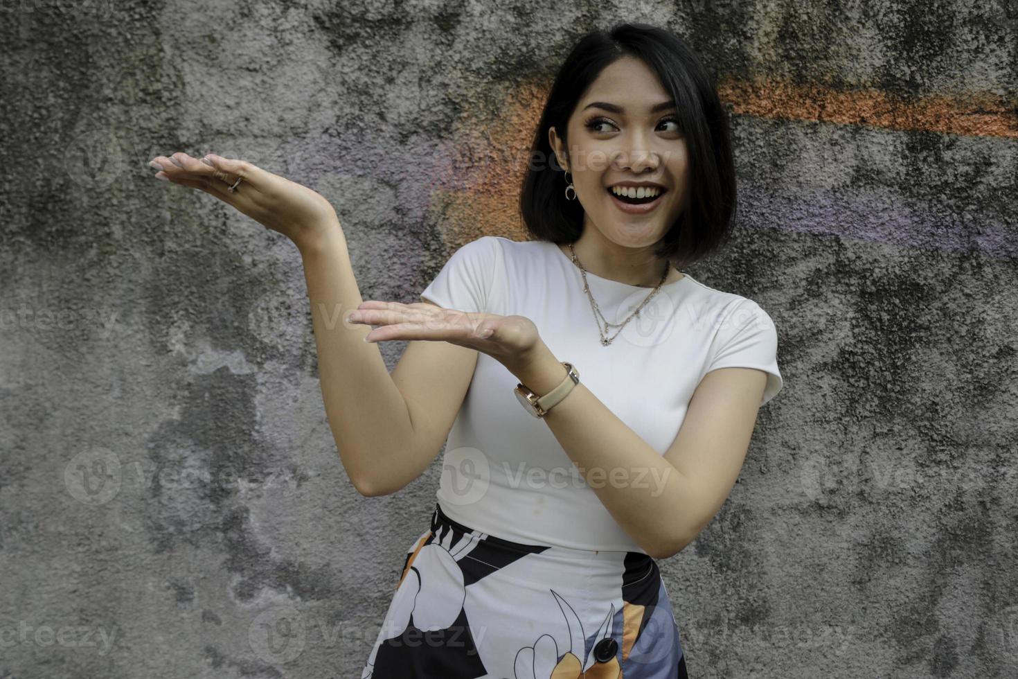 visage heureux et souriant avec le sourire d'une jeune fille asiatique avec un point de main sur un espace vide. photo