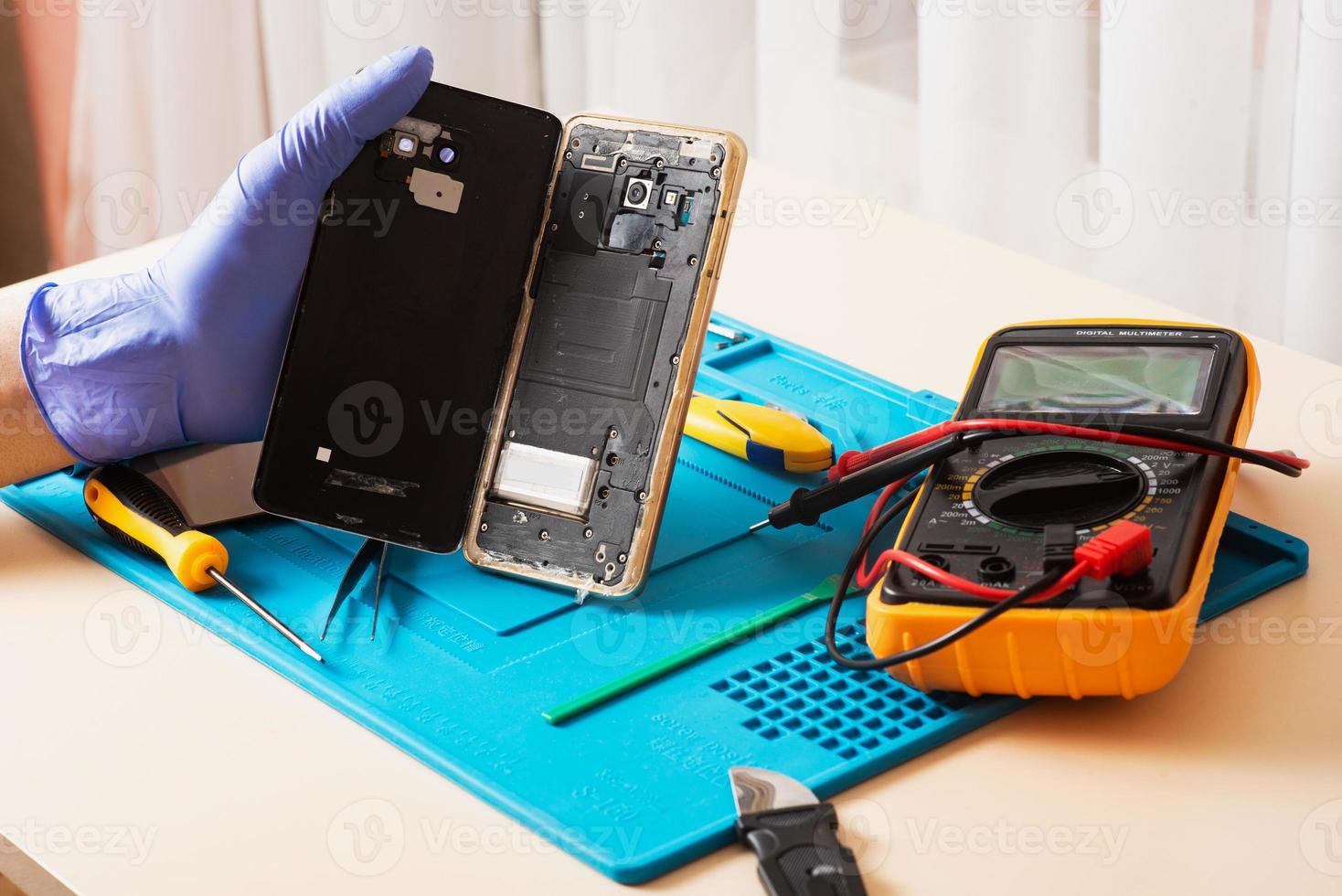 artisan en gants de caoutchouc répare ou entretient un téléphone portable sur un tapis en caoutchouc spécial pour réparation. vue de l'intérieur photo