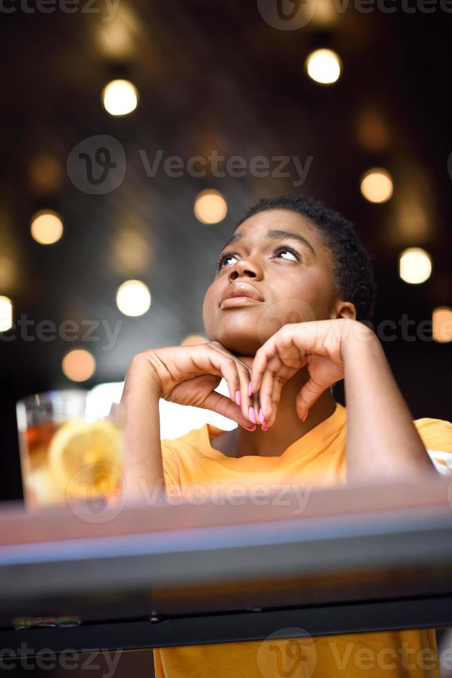 jeune femme noire aux cheveux très courts prenant un verre de thé froid. photo