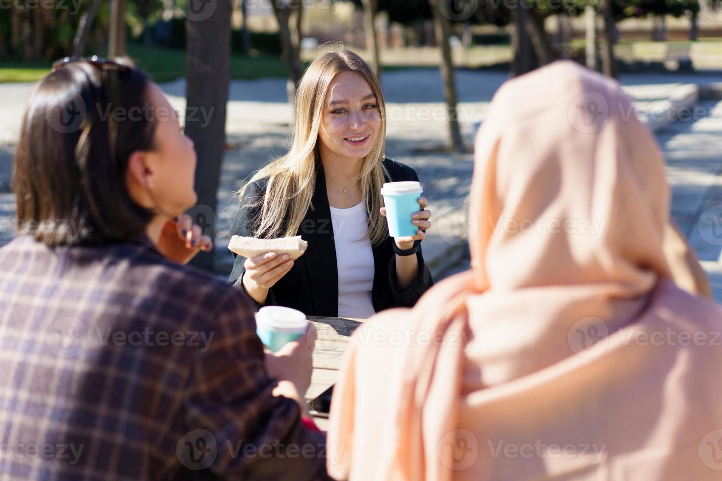 trois filles diverses ayant une pause-café et bavardant dans le parc de la ville photo