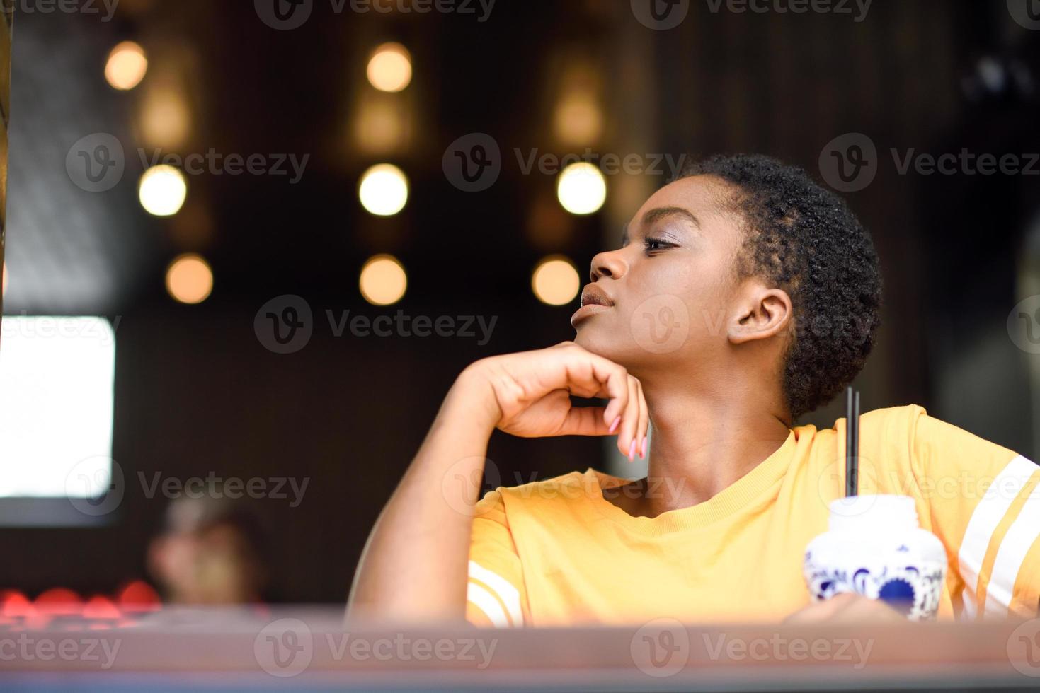 jeune femme noire aux cheveux très courts prenant un verre de thé froid. photo