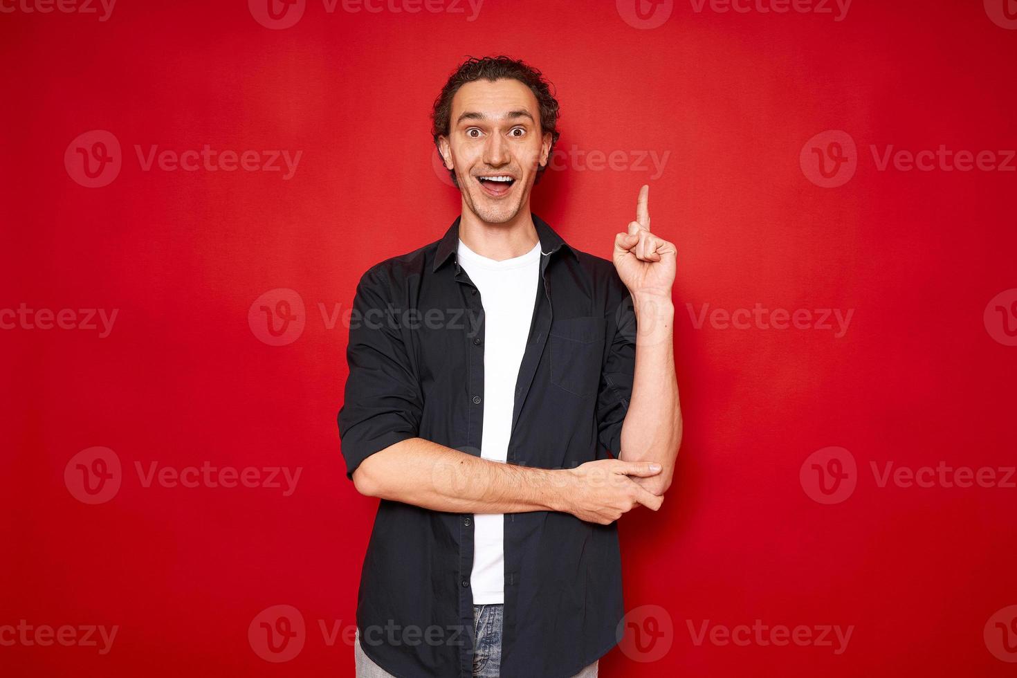 un homme excité avec la bouche ouverte pointe l'index vers le haut, se réjouit d'une nouvelle idée brillante. vêtu de vêtements décontractés isolés sur un espace de fond rouge pour le texte. concept - remue-méninges, connaissances, inspiration photo