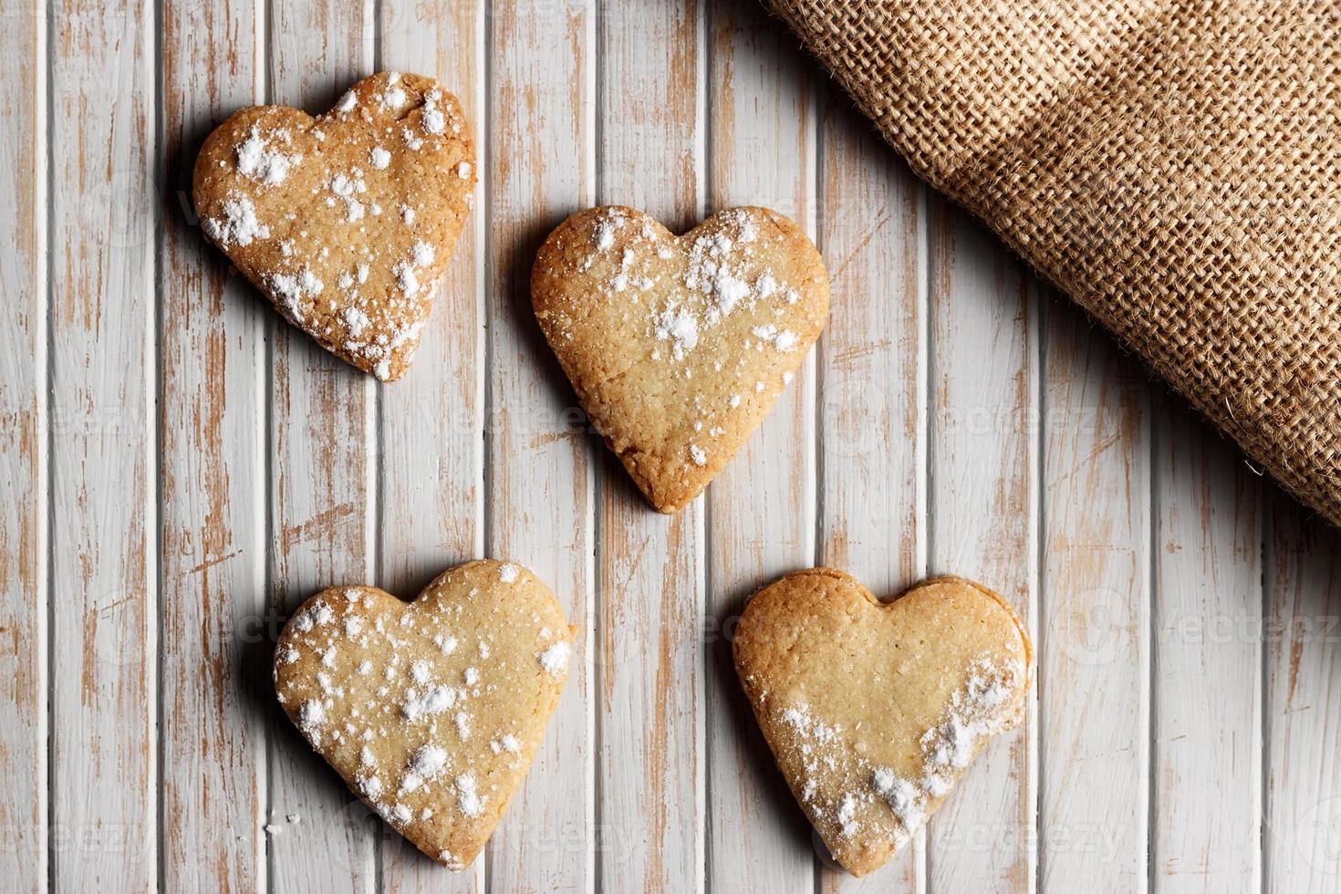 délicieux biscuits faits maison en forme de cœur saupoudrés de sucre glace sur une planche de bois. image horizontale vue du dessus. photo