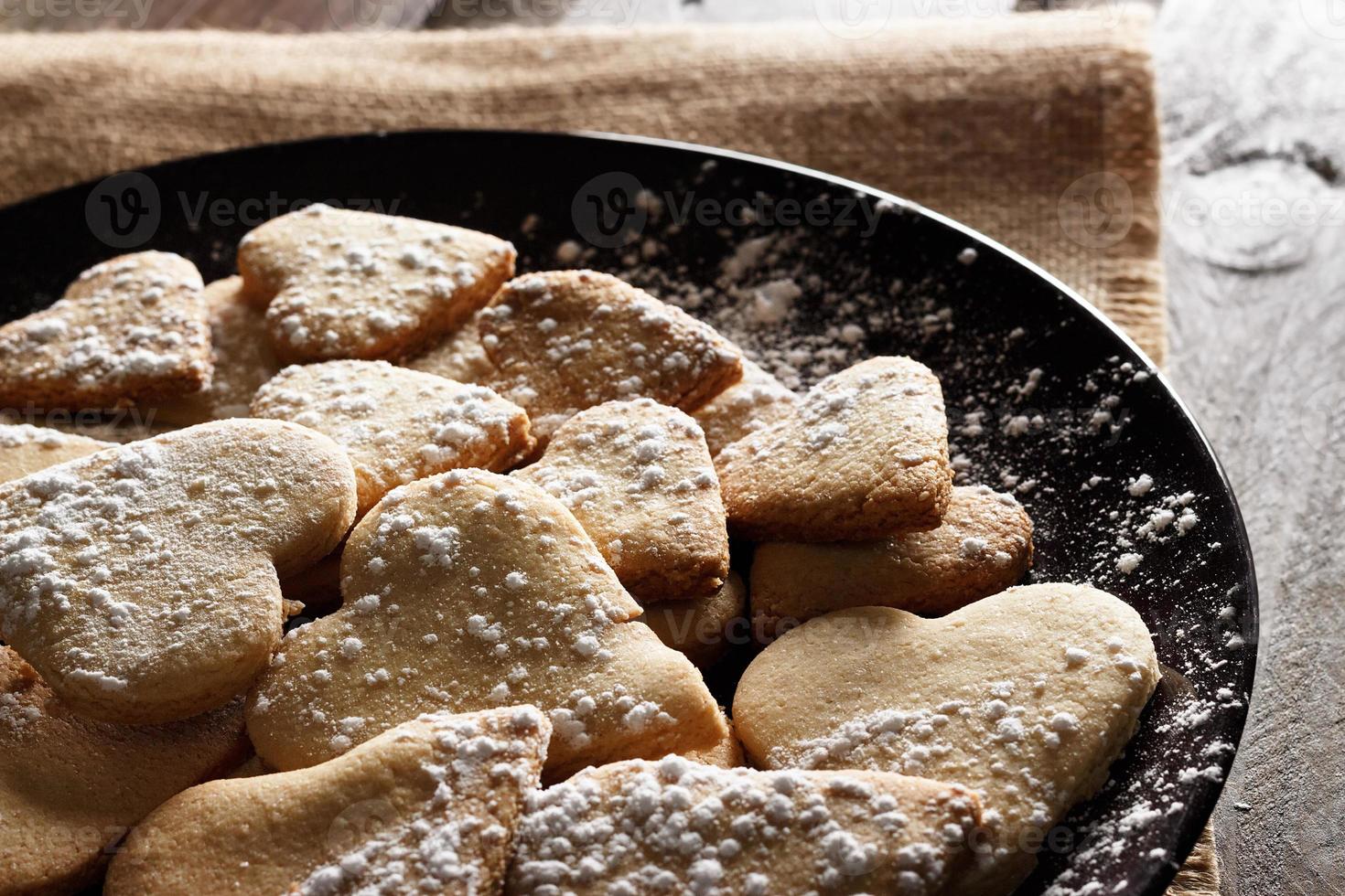 de délicieux biscuits faits maison en forme de cœur saupoudrés de sucre glace sur un sac et des planches de bois. image horizontale vue en contre-jour. photo