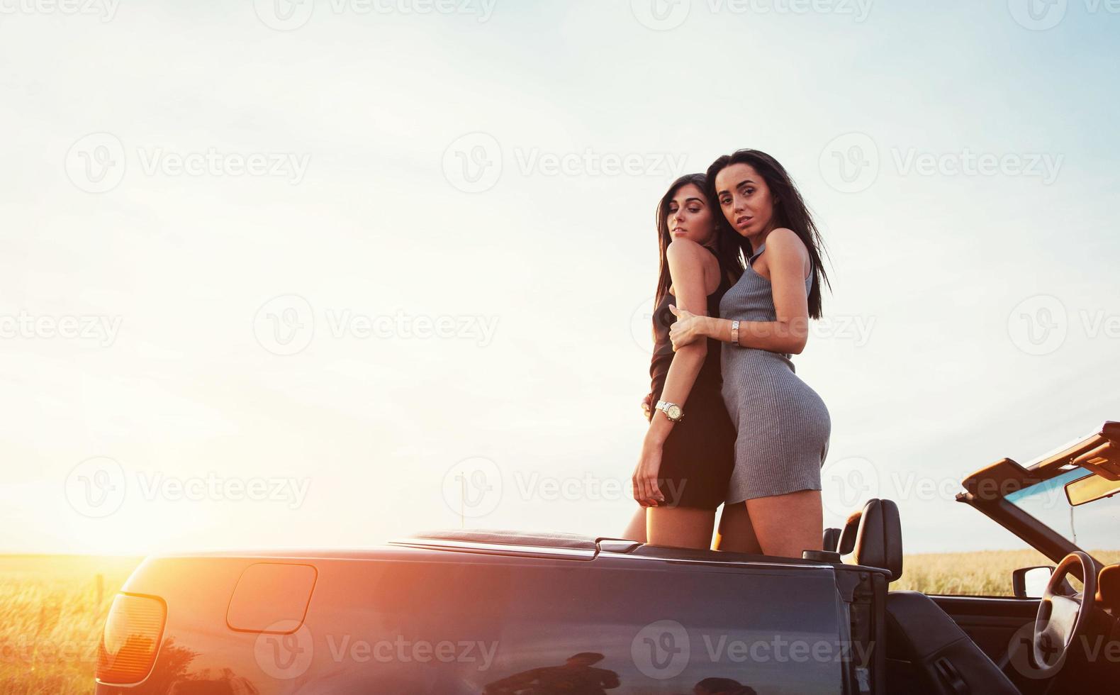 deux filles heureuses de poser à côté d'une voiture noire photo