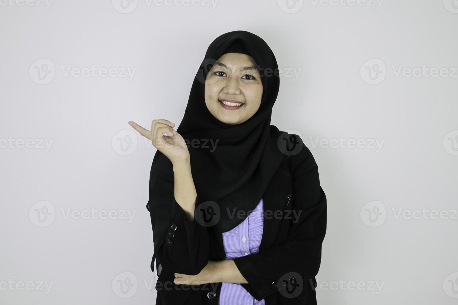 heureuse jeune femme islamique asiatique portant un foulard est souriante et pointant à côté. photo