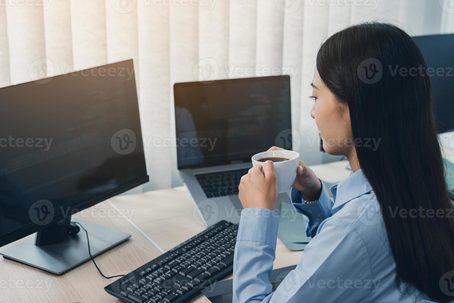 une femme asiatique buvait du café tôt le matin tout en contemplant le programme et le code sur l'écran de l'ordinateur. photo