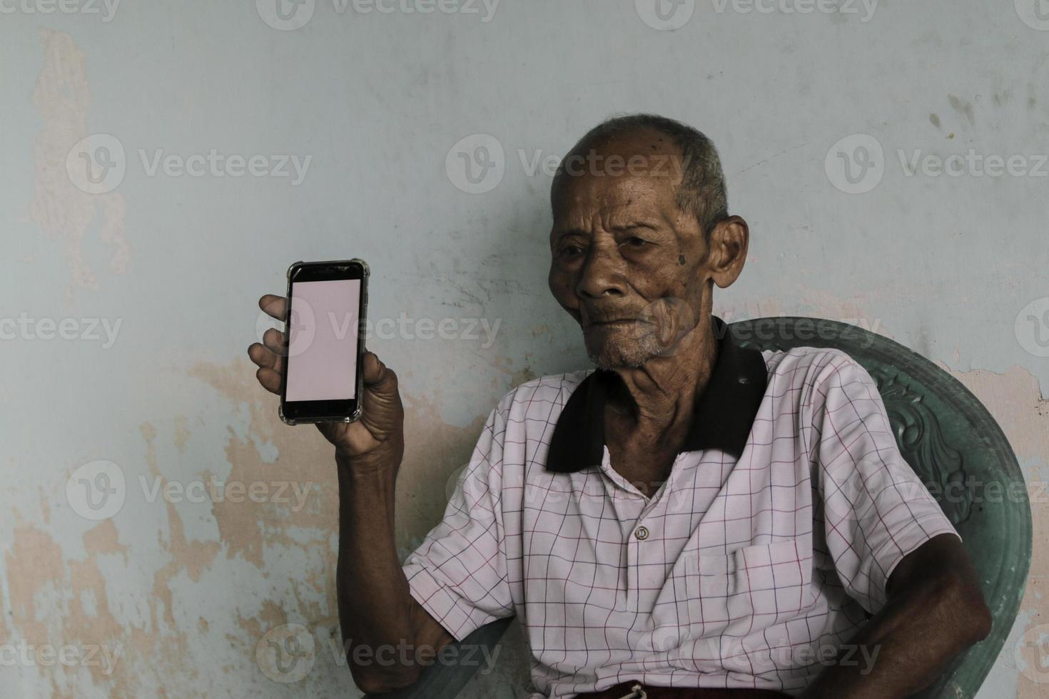 un portrait d'un vieux grand-père indonésien montrant un smartphone à écran blanc. photo