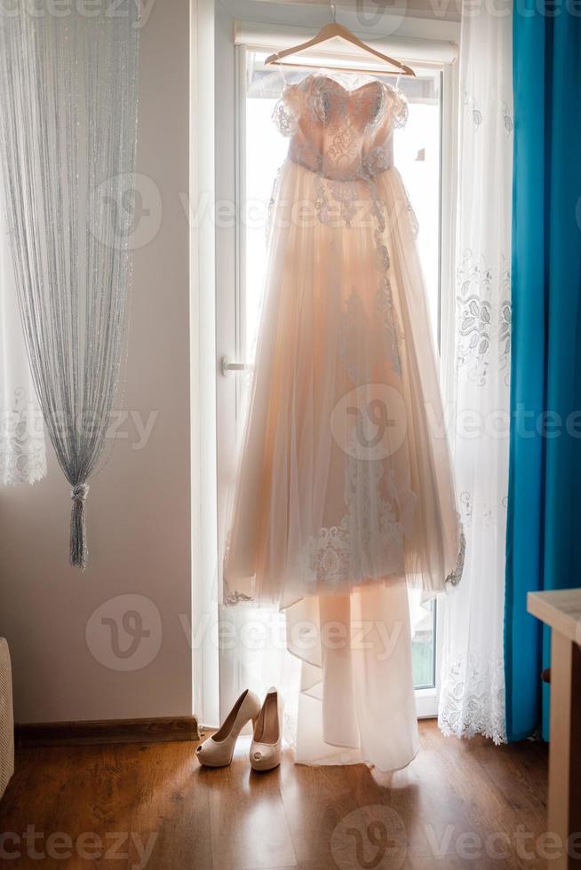 préparation du matin de la mariée. belle robe longue blanche de mariage et chaussures de hautes collines sur fond de grande fenêtre à la maison. Jour de mariage photo