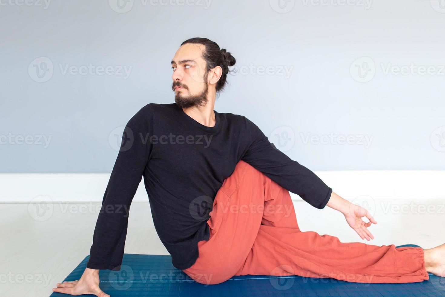 jeune homme blanc aux cheveux longs caucasien fait du yoga dans un studio ou une maison. photo